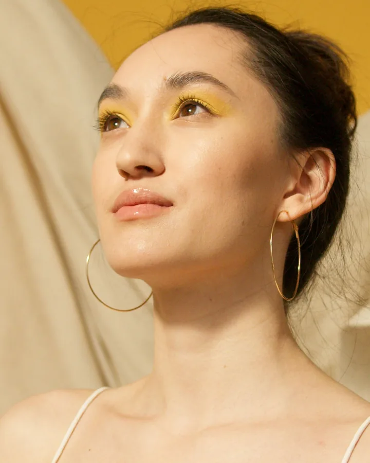 Model with a wash of yellow eyeshadow and gold hoops against a cream backdrop