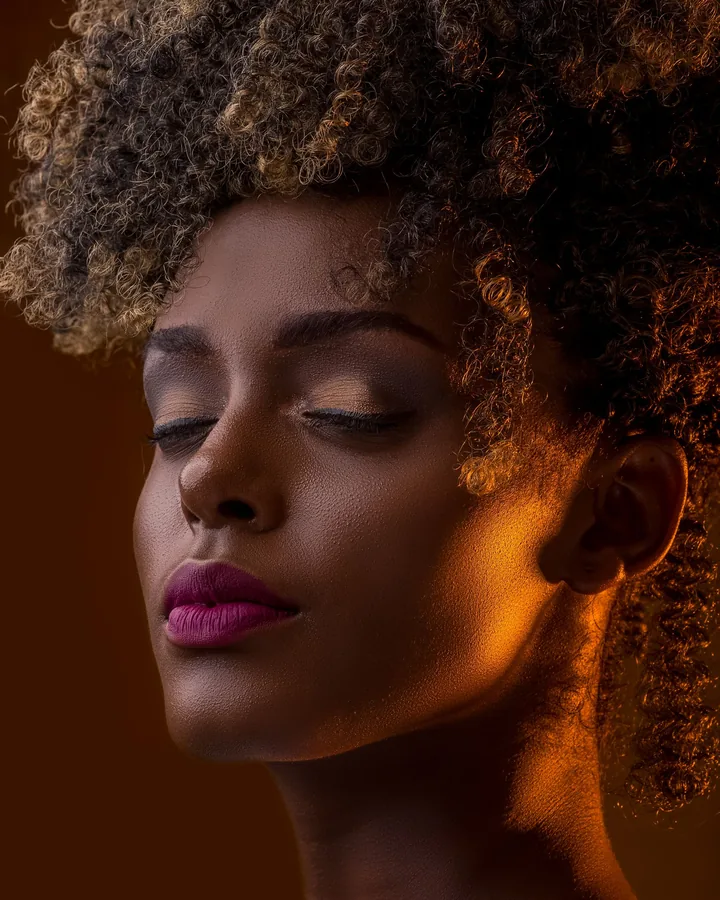 Model with curly hair, a plum lip and warm side light