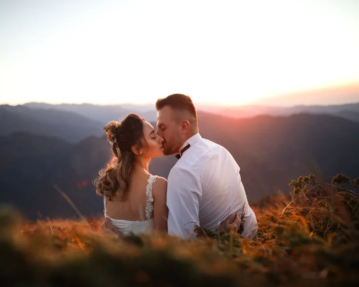 Bride and groom kissing on a hillside at sunset above the mountains