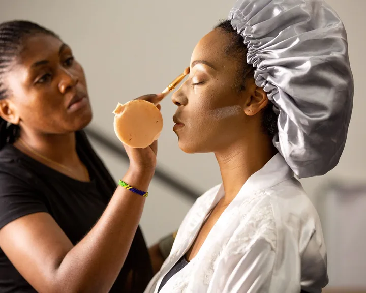 Makeup artist pressing foundation onto a client wearing a satin bonnet