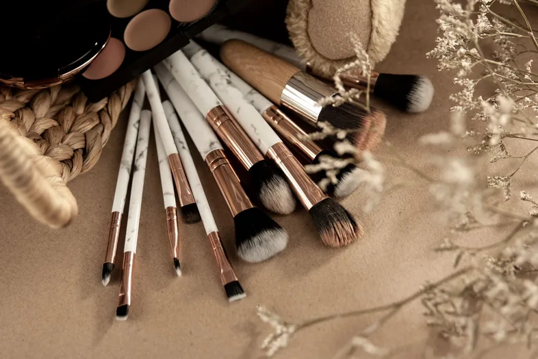 Makeup brushes and an eyeshadow palette laid out on a beige surface with dried flowers