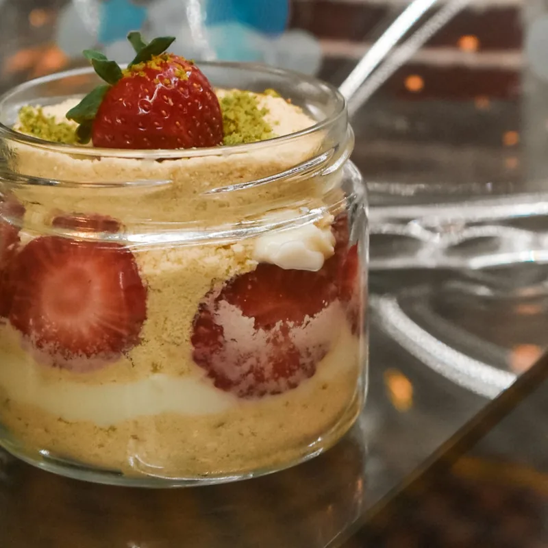 Glass jar layered with sponge cake, cream and sliced strawberries, topped with a whole strawberry