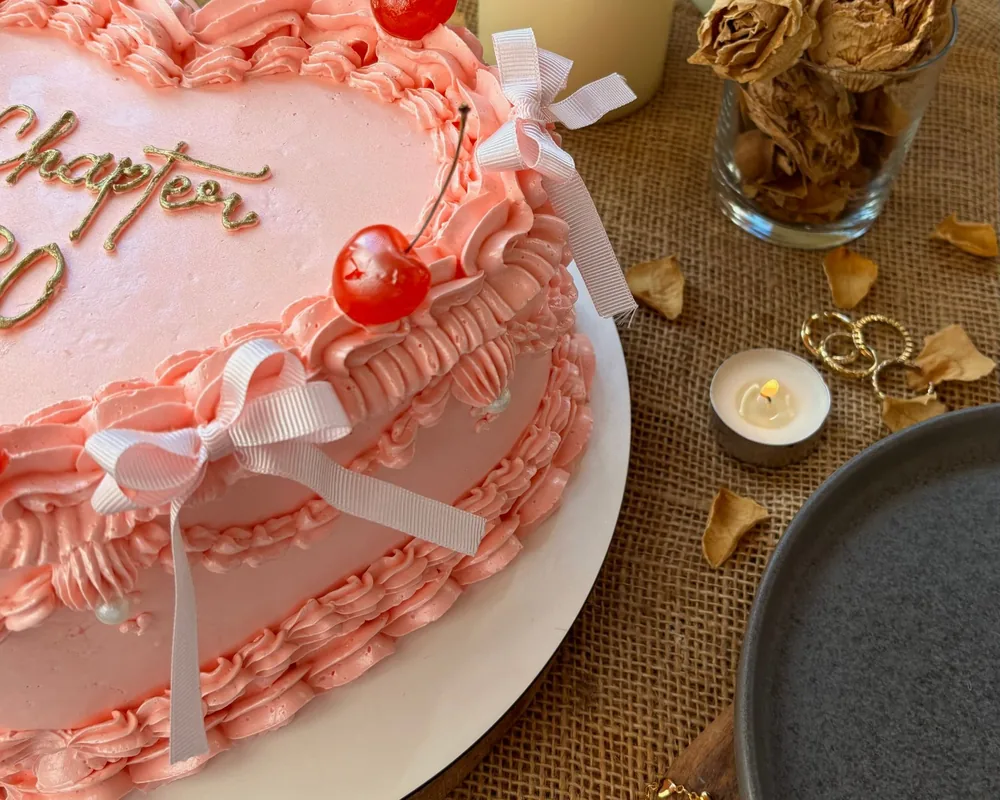 Pink heart cake with ruffled buttercream borders, white ribbon bows and glossy cherries