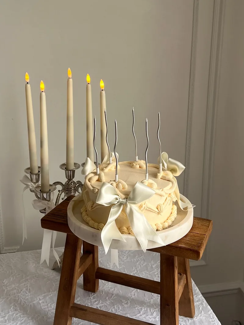 Ivory cake tied with satin bows on a small wooden stool beside tall candles
