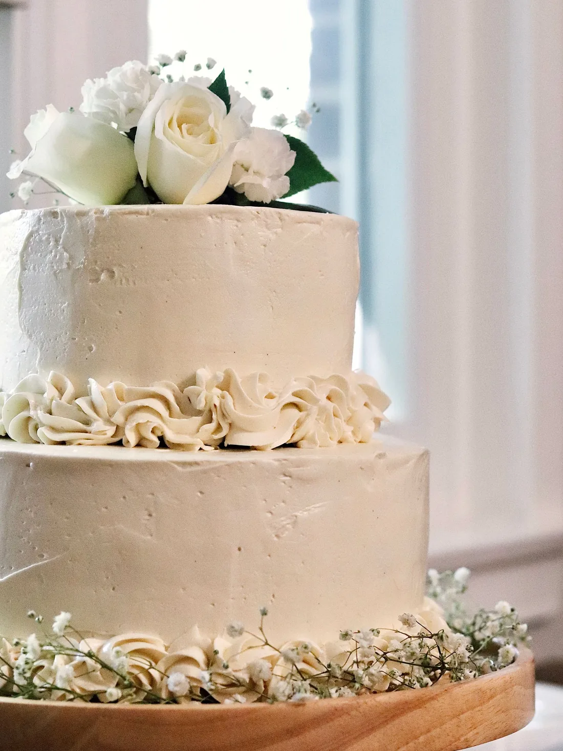 Two-tier ivory buttercream wedding cake with a ring of piped rosettes, baby's breath and white roses on top