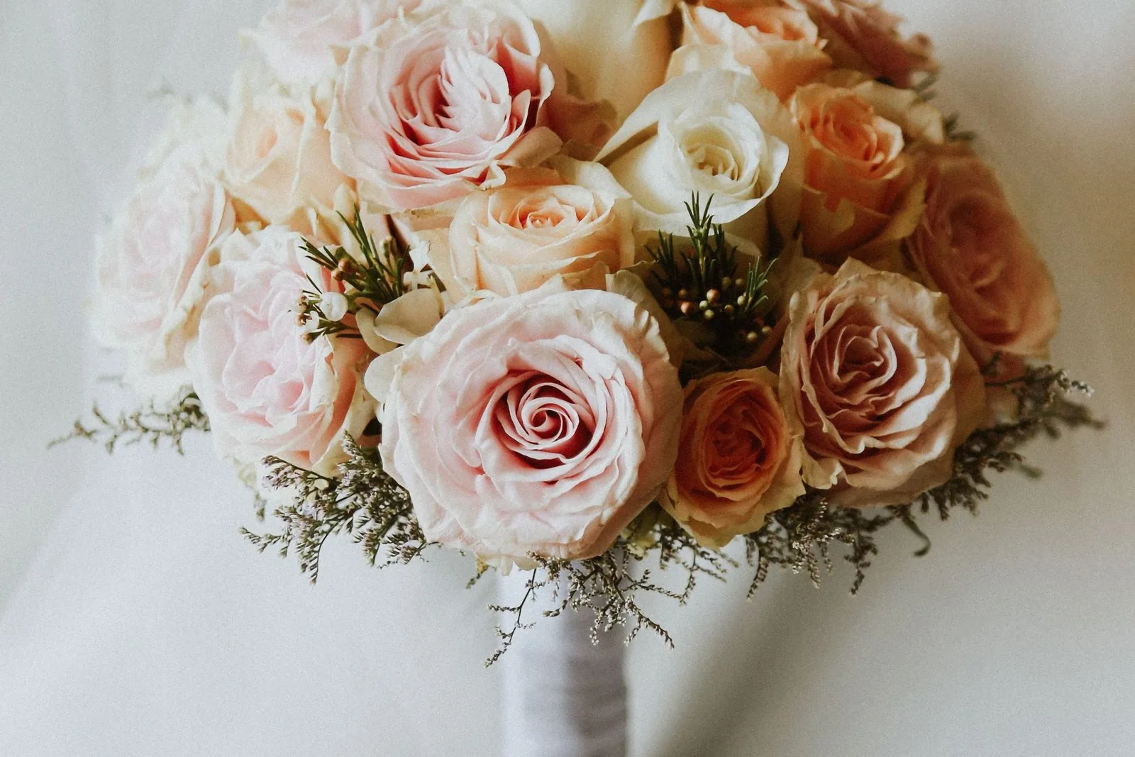 Bridal bouquet of blush, cream and apricot garden roses on white satin