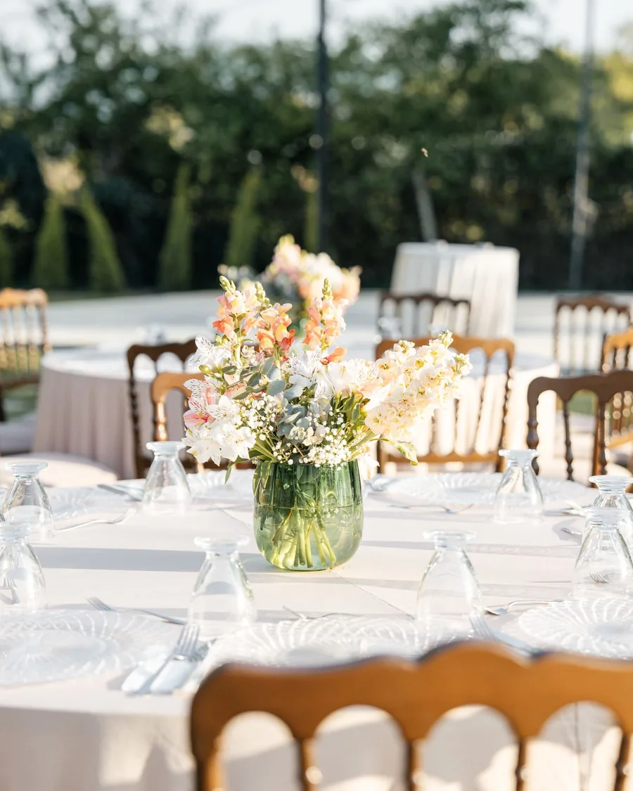 Round reception table with a peach and cream centerpiece in a glass vase, garden behind