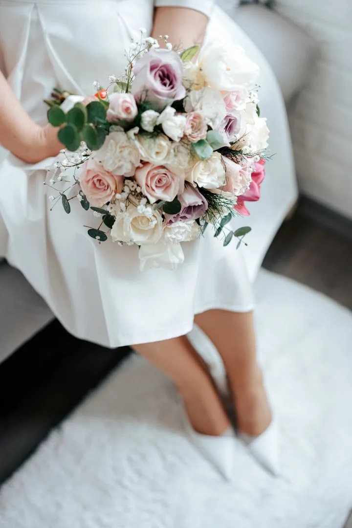 Bride seated with a round bouquet of white, blush and mauve roses
