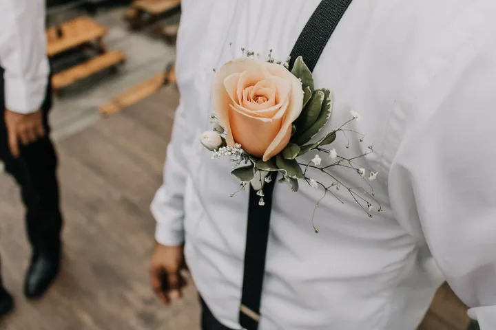Peach rose boutonniere on a white shirt with black suspenders