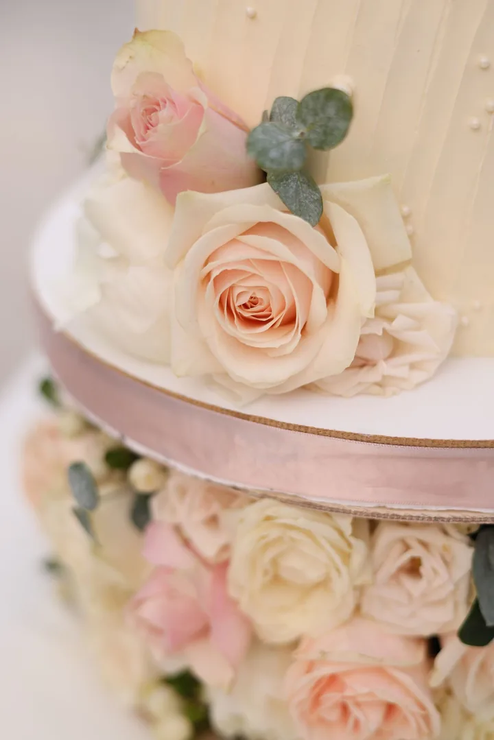 White wedding cake with blush roses and eucalyptus on a ribboned stand
