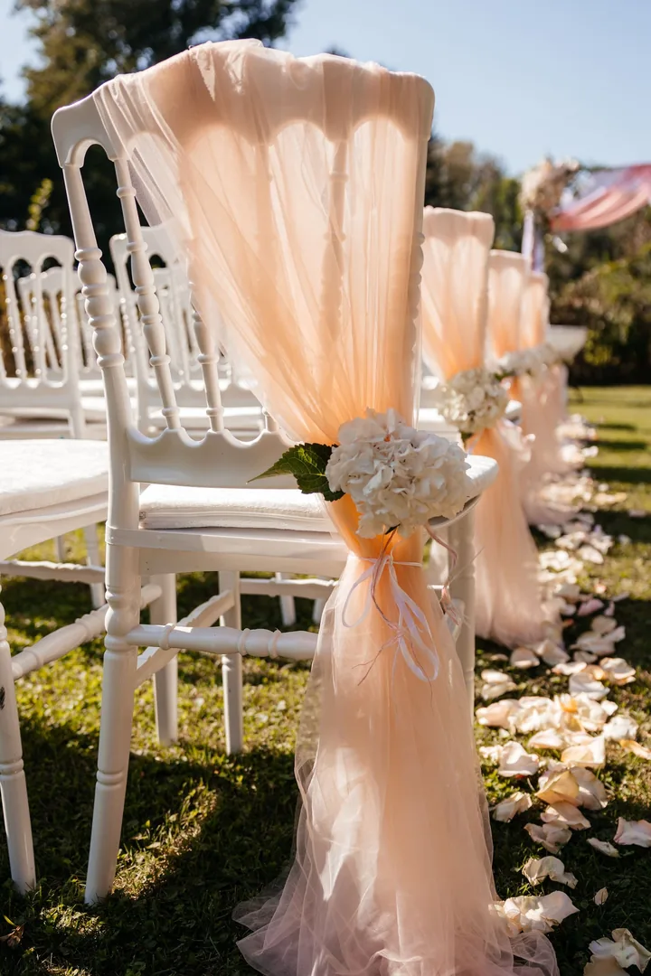 White aisle chairs draped in peach chiffon with hydrangea ties and scattered petals
