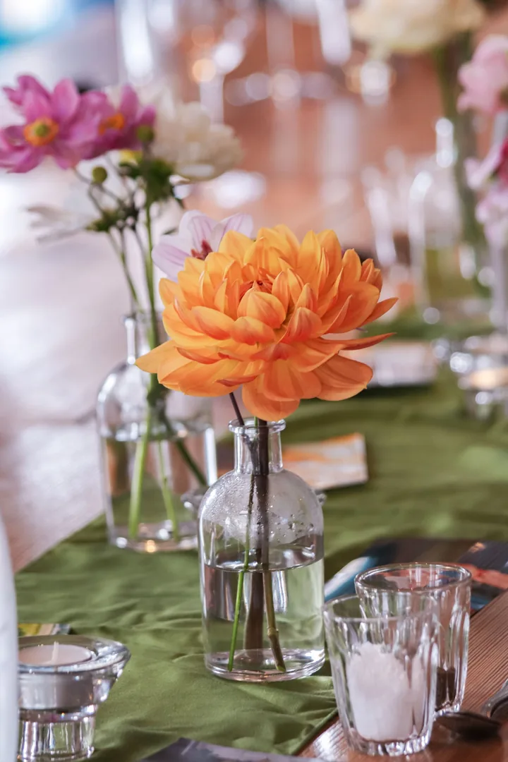 Orange dahlia and pink cosmos in glass bud vases on a moss-green runner