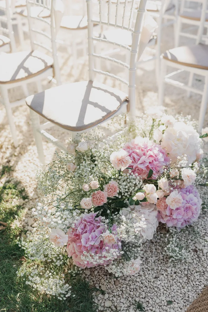 Meadow of pink hydrangea and baby's breath at the foot of white ceremony chairs