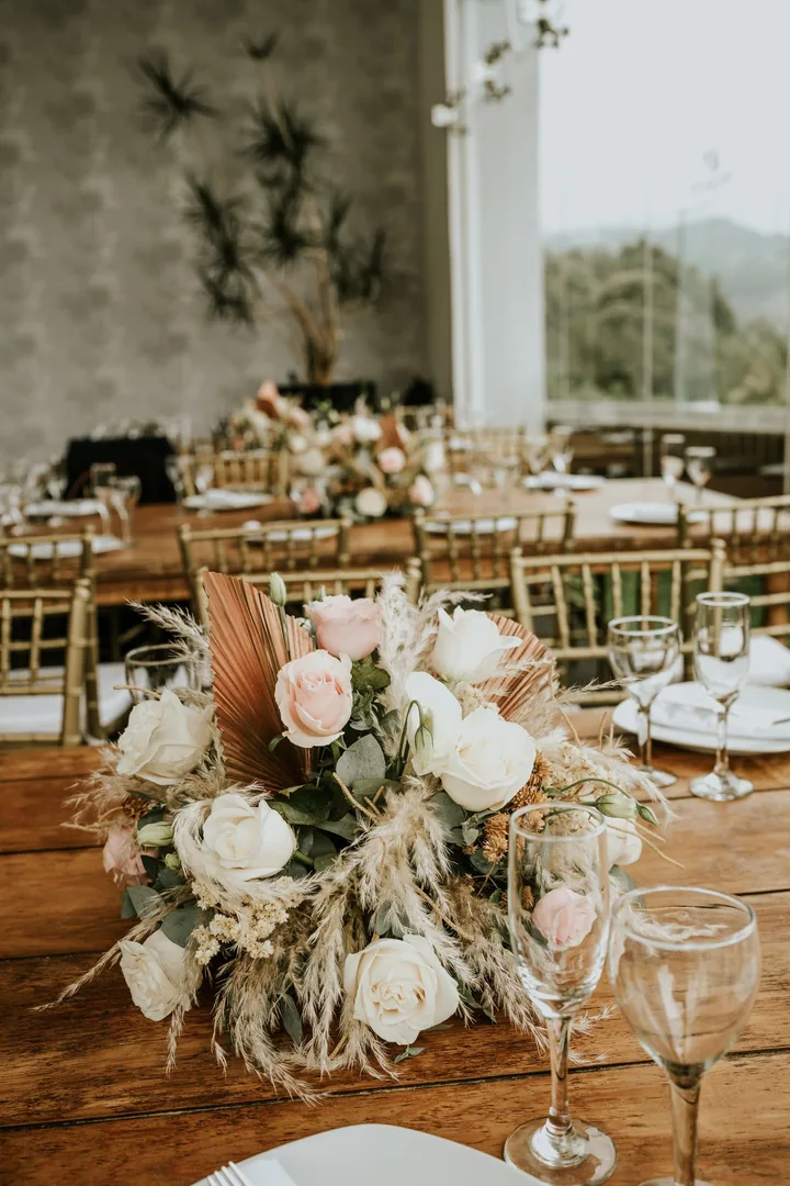 Centerpiece of white and blush roses with pampas and dried palm on a wooden table