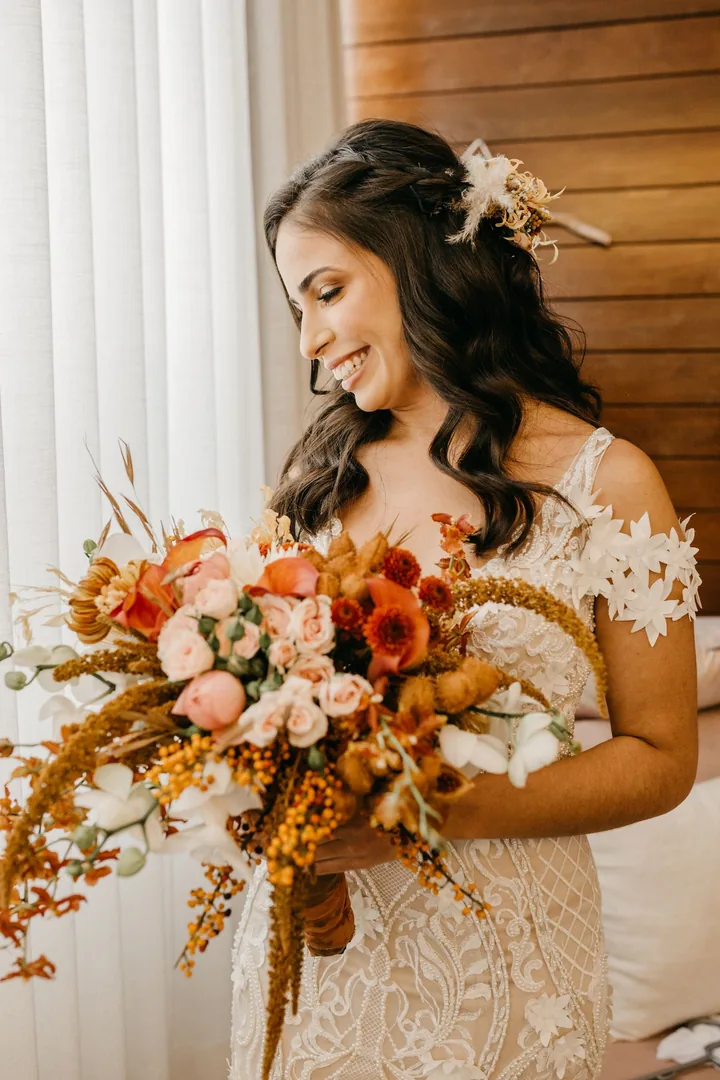 Smiling bride holding a trailing bouquet of rust, apricot and blush flowers with dried grasses