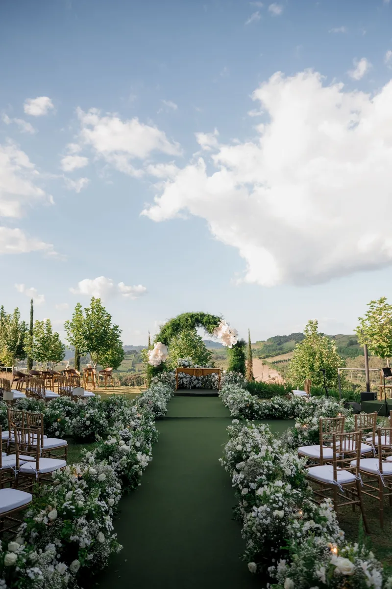 Green aisle lined with low white flowers leading to the arch under a blue sky