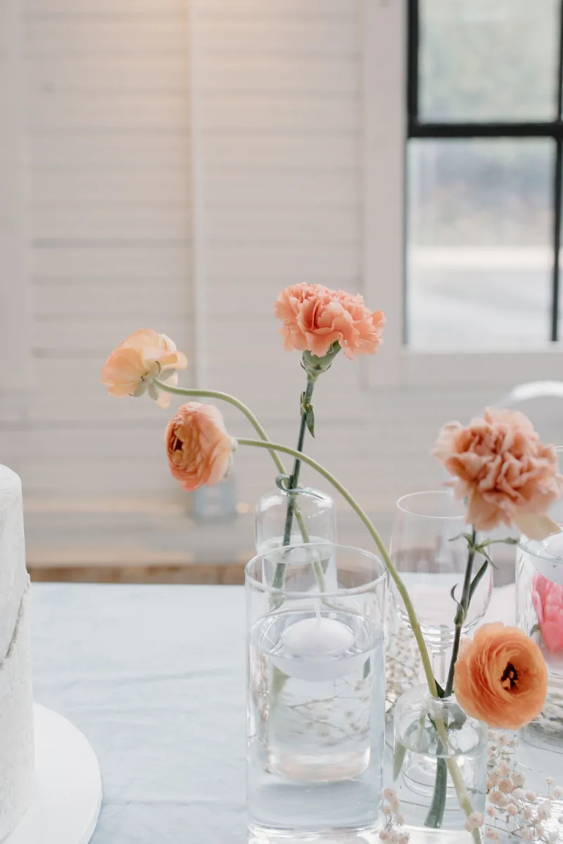 Single peach carnations and ranunculus in clear bud vases with floating candles