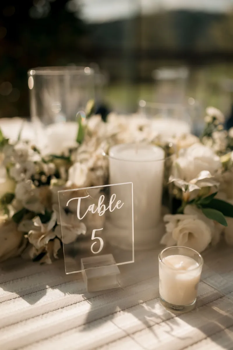 Acrylic table number among white roses and candles in soft afternoon light