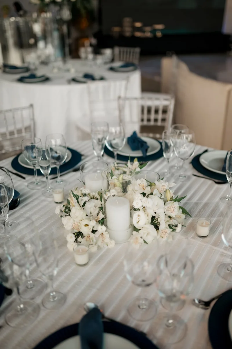 Round table with a ring of white flowers around a pillar candle, navy napkins and glassware