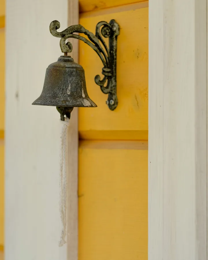 Small brass bell mounted beside a yellow door