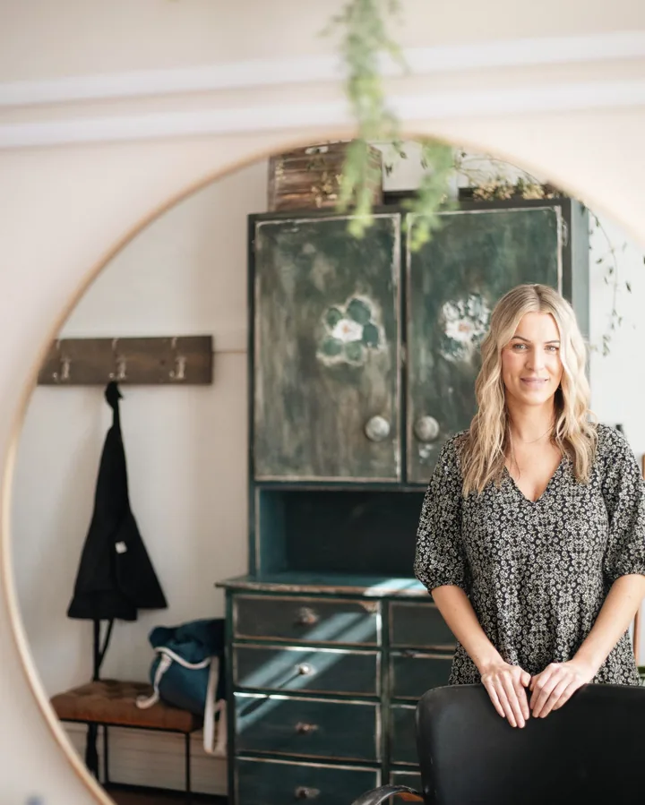 Tess at her styling chair, reflected in a large round mirror