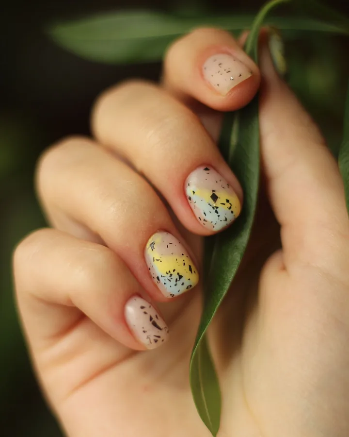 Short nude nails with black speckles and a yellow fade