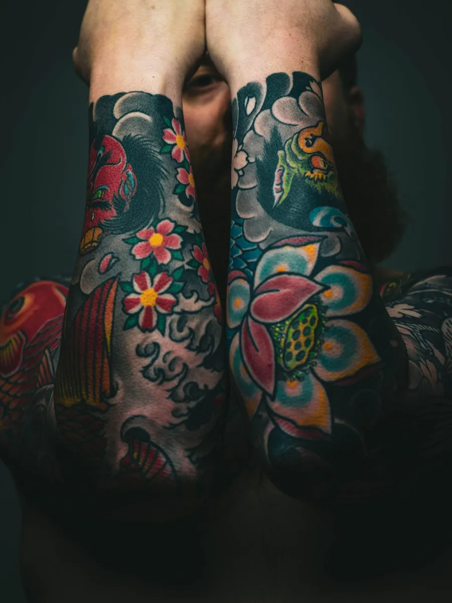 Two forearms covered in bright colour work by Kai
